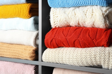 Many knitted winter clothes stacked on shelves, closeup