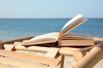 Photo of Book on wooden deck chair at seaside. Reading while vacation