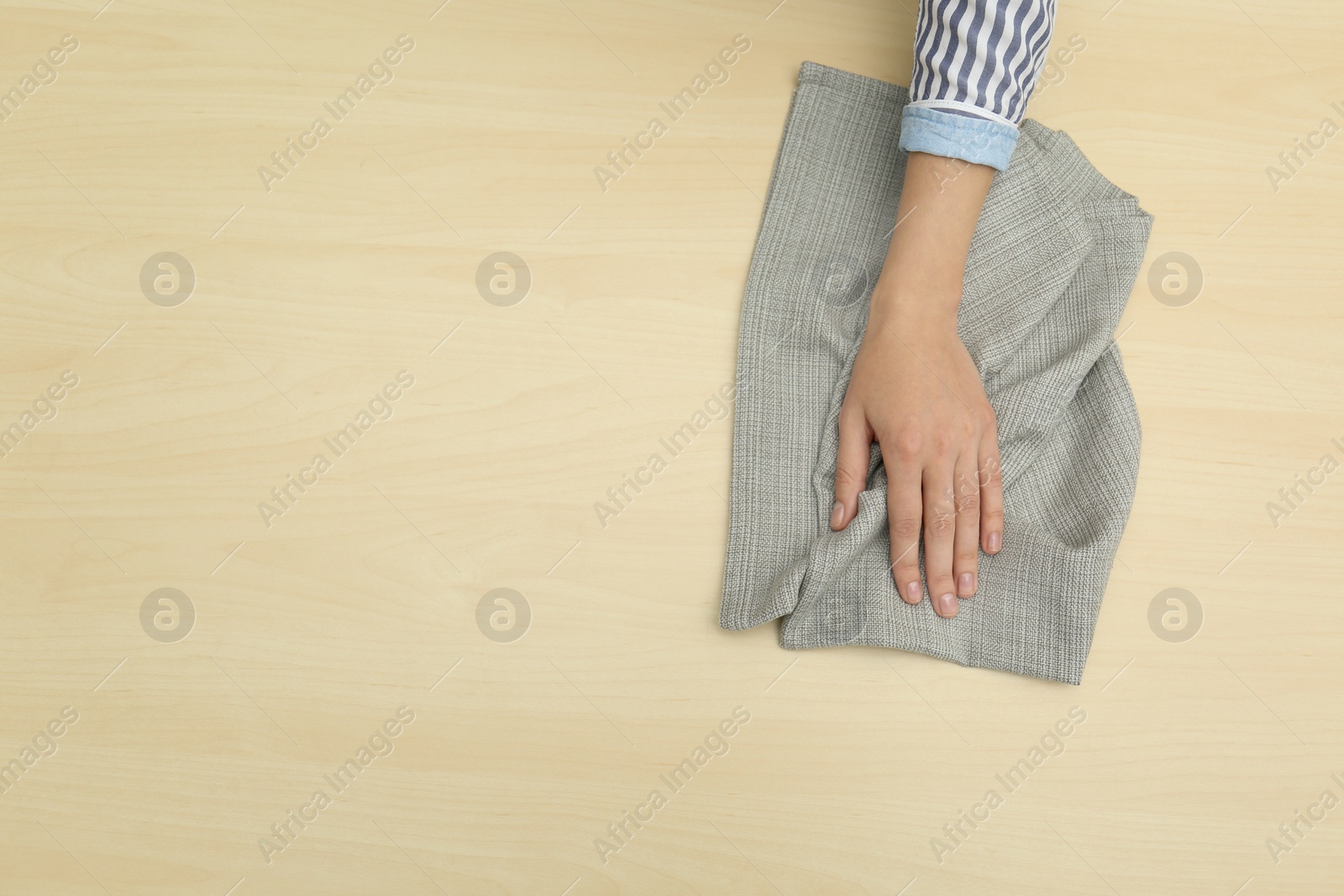 Photo of Woman wiping wooden table with kitchen towel, top view. Space for text