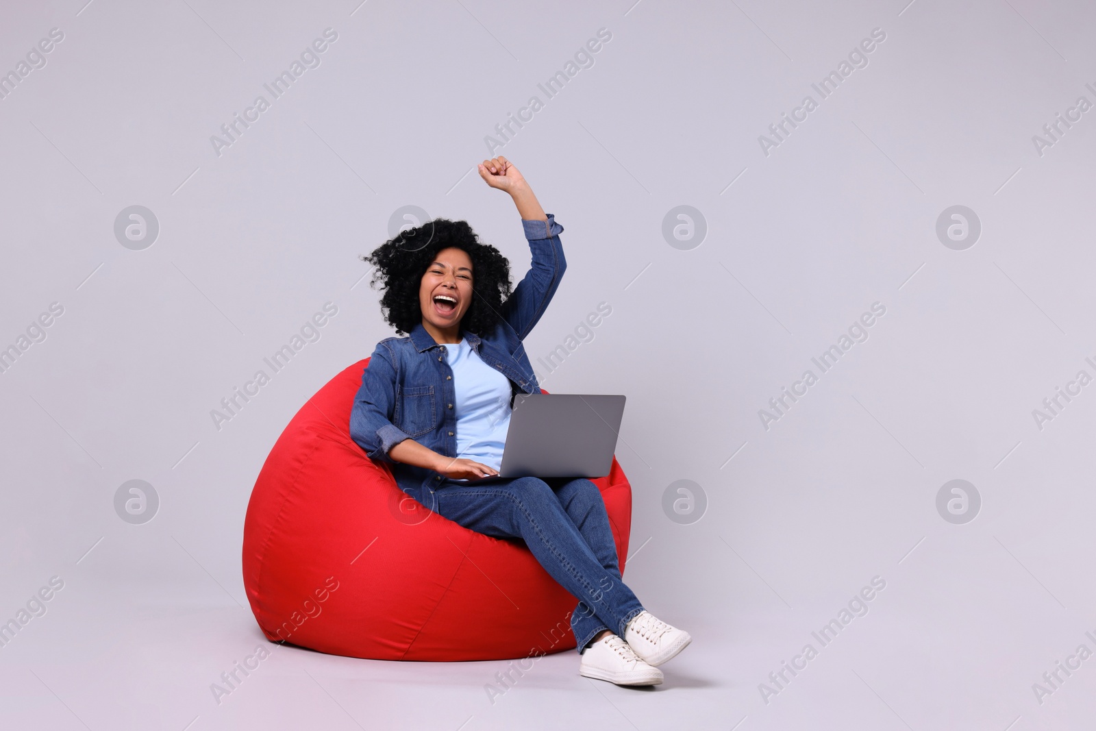 Photo of Emotional young woman with laptop sitting on beanbag chair against light grey background