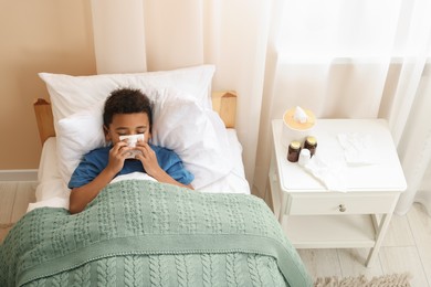 Photo of African-American boy with scarf and tissue blowing nose in bed indoors, above view. Cold symptoms