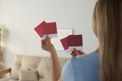 Photo of Woman choosing paint shade for wall in room, focus on hands with color sample cards. Interior design