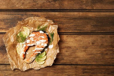 Photo of Tasty salmon steak with sauce, citrus slices and herbs on wooden table, top view. Space for text