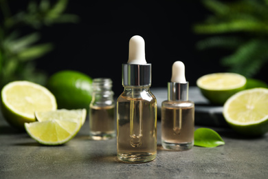 Photo of Lime essential oil and cut citrus fruits on grey table