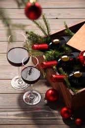 Wooden crate with bottles of wine, glasses, fir twigs and red Christmas balls on table