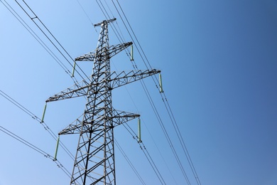 Photo of High voltage tower with electricity transmission power lines against blue sky, low angle view