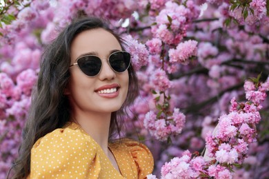 Stylish woman in sunglasses near blossoming sakura tree on spring day