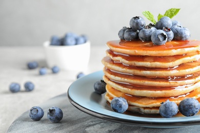 Photo of Plate of delicious pancakes with fresh blueberries and syrup on grey table, closeup. Space for text