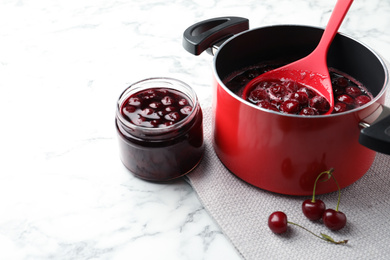 Pot with cherries in sugar syrup on white marble table. Making delicious jam