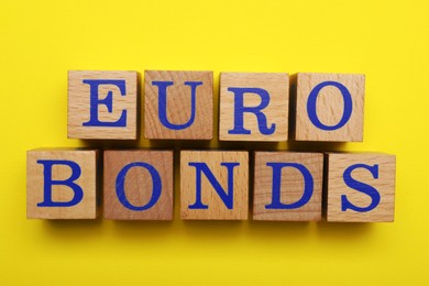 Photo of Word Eurobonds made of wooden cubes with letters on yellow background, flat lay