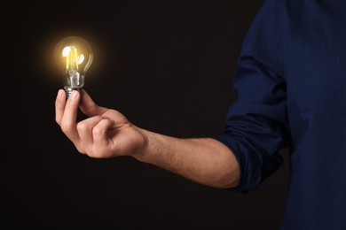 Photo of Glow up your ideas. Closeup view of man holding light bulb on black background