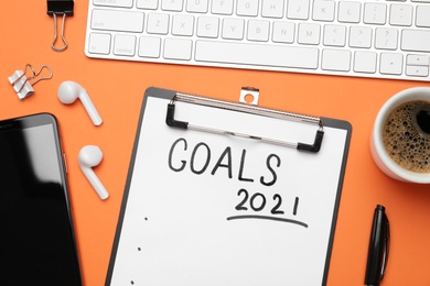 Photo of Paper with inscription 2021 Goals, new year items. Objects on orange background, flat lay