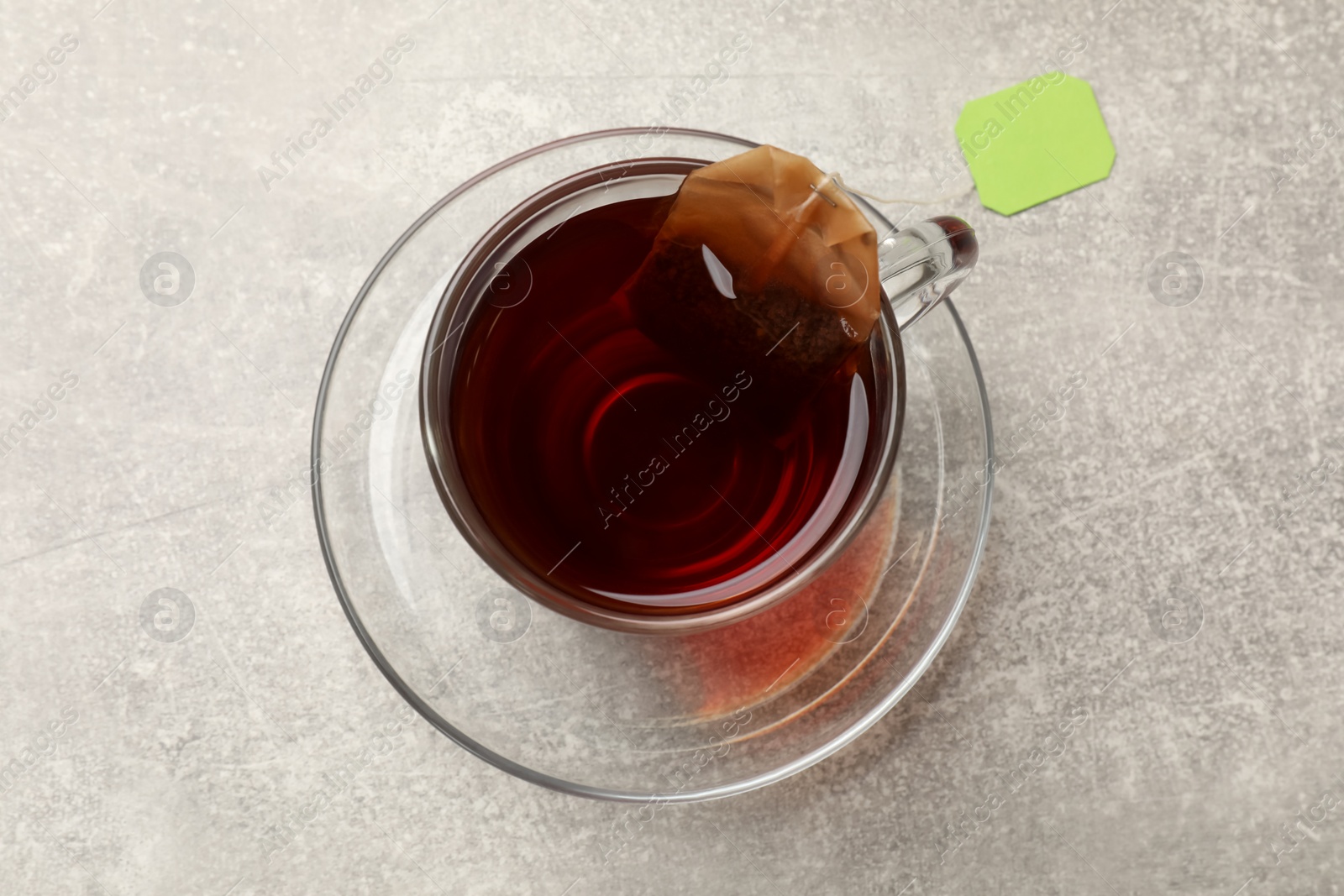 Photo of Brewing tea. Glass cup with tea bag on light table, top view