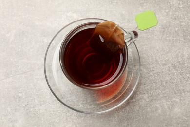 Photo of Brewing tea. Glass cup with tea bag on light table, top view
