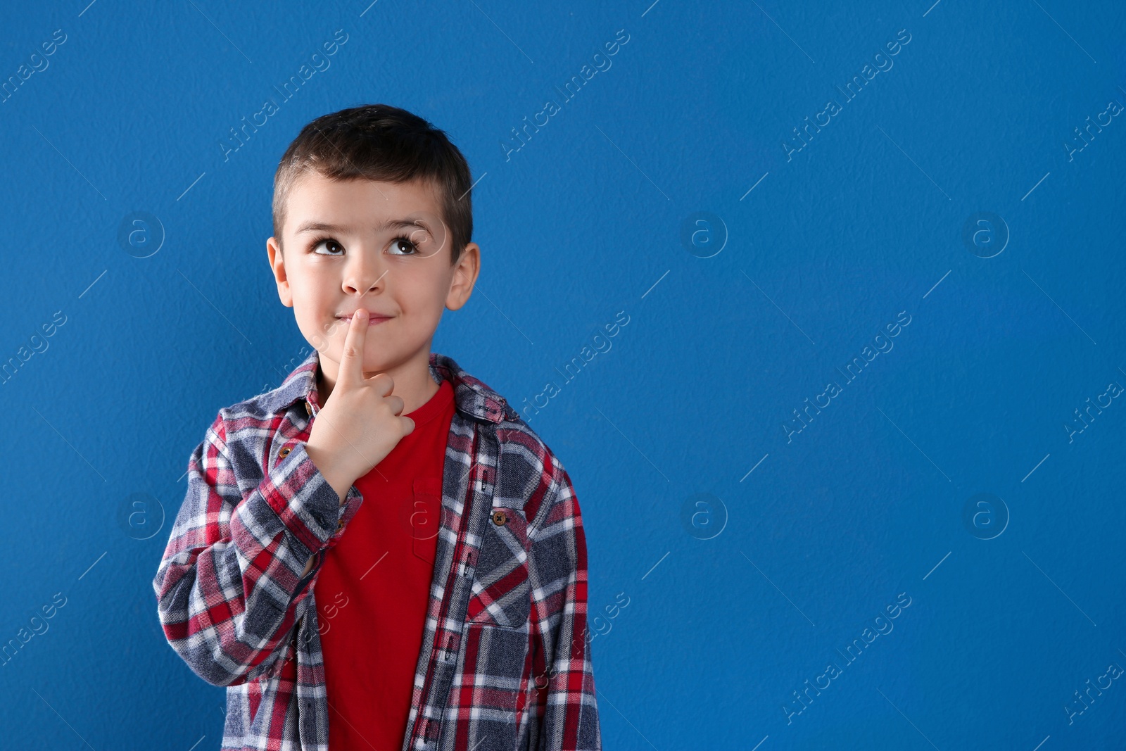 Photo of Thoughtful little boy on blue background, space for text