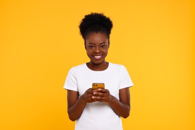 Photo of Happy young woman with smartphone on orange background