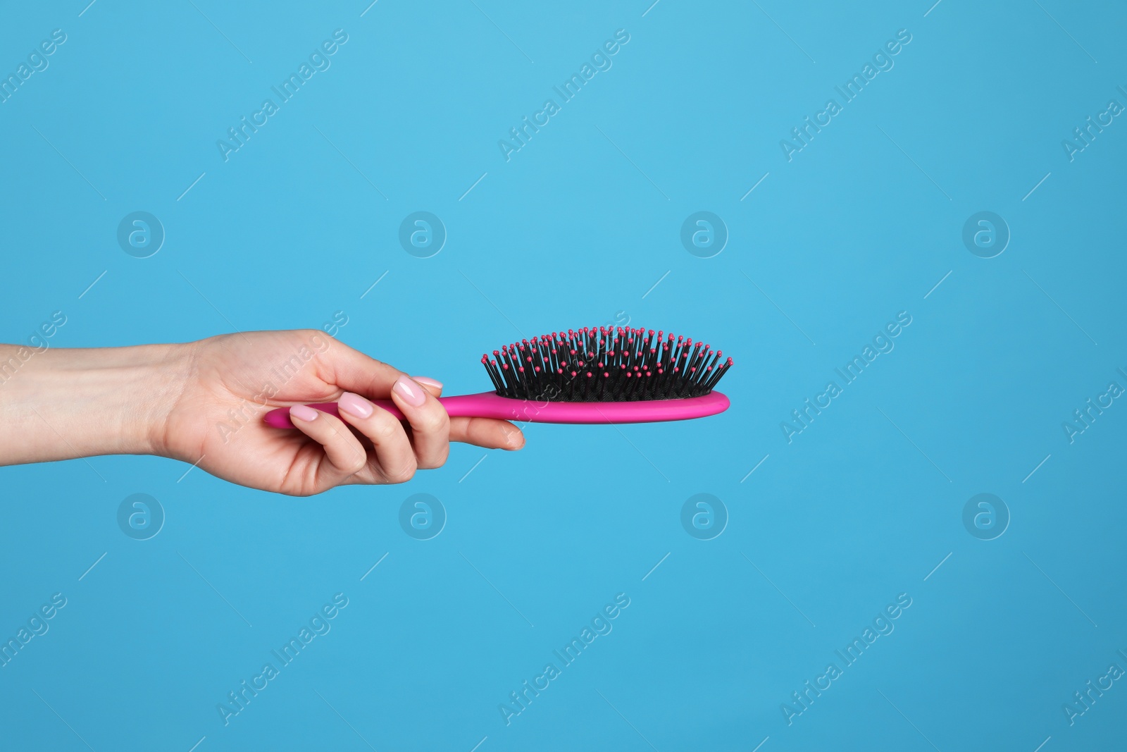 Photo of Woman holding hair brush against blue background, closeup