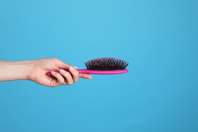 Photo of Woman holding hair brush against blue background, closeup