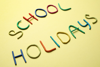 Text School Holidays made of modelling clay on yellow background