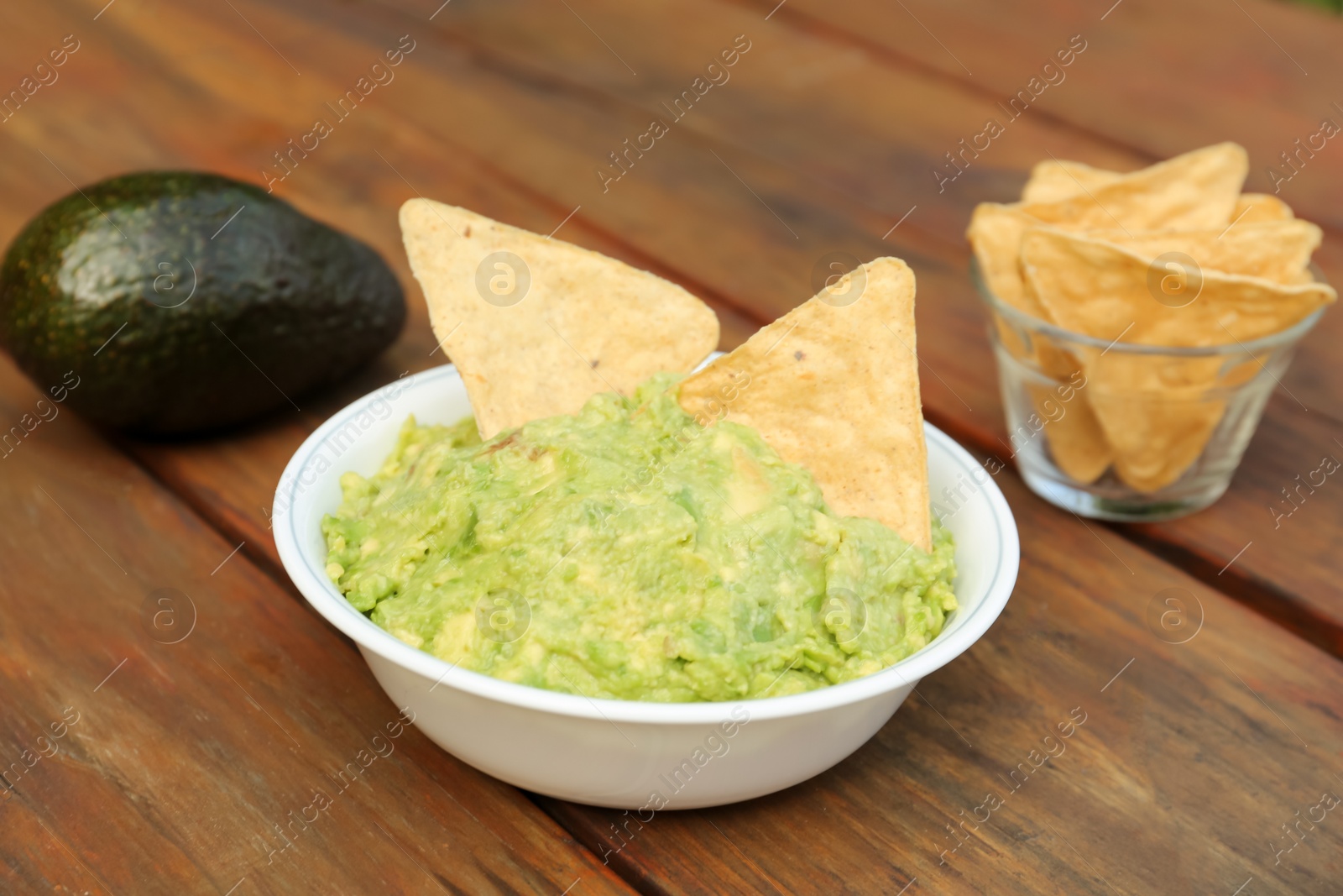 Photo of Delicious guacamole, avocado and nachos on wooden table, closeup