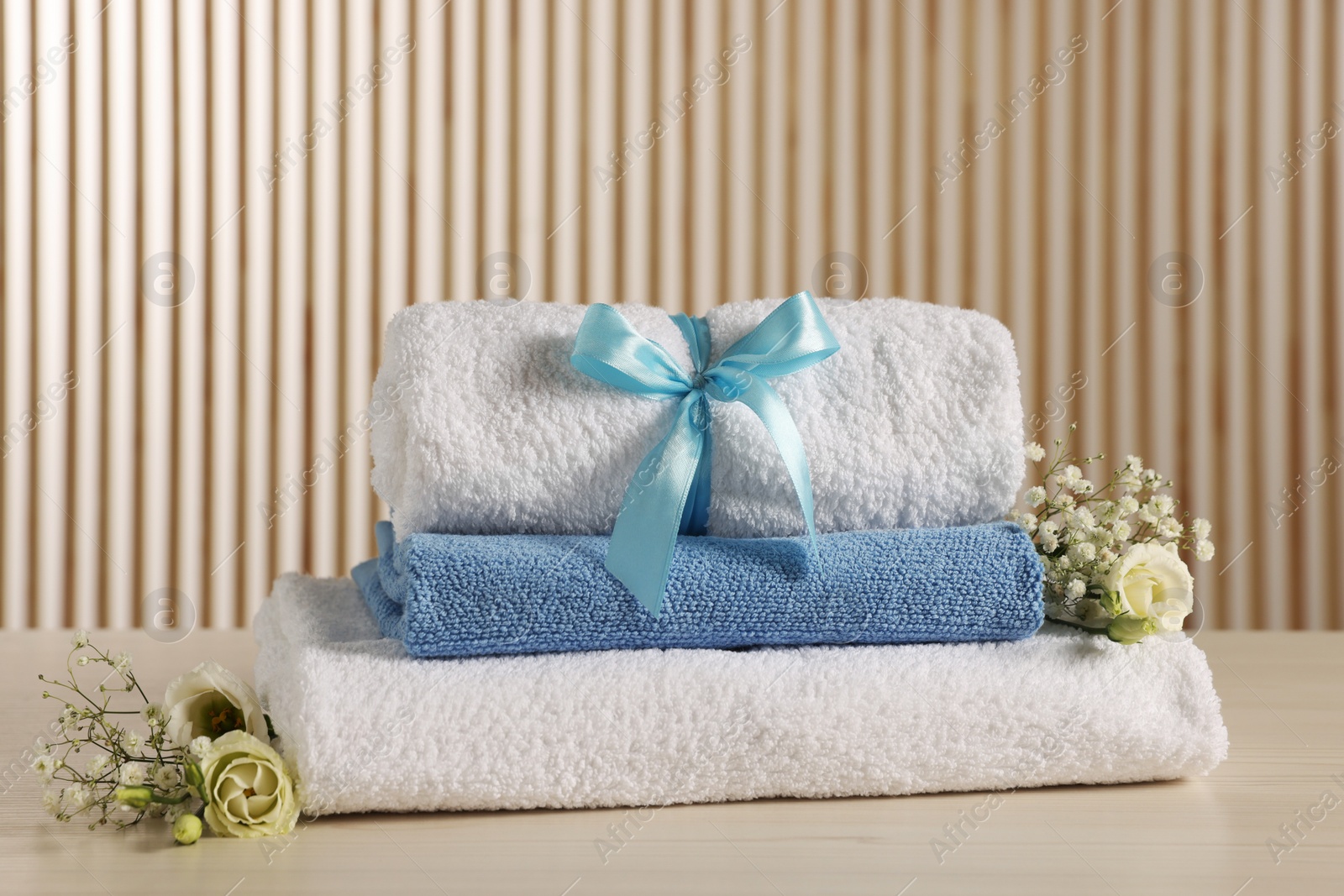 Photo of Soft towels, gypsophila and eustoma flowers on light wooden table