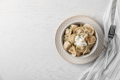 Photo of Tasty dumplings with sour cream in bowl on white wooden table, flat lay. Space for text