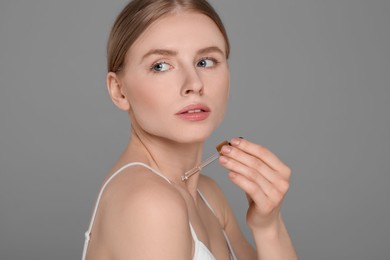 Photo of Beautiful young woman applying essential oil onto shoulder on grey background