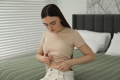 Photo of Diabetes. Woman making insulin injection into her belly on bed in room