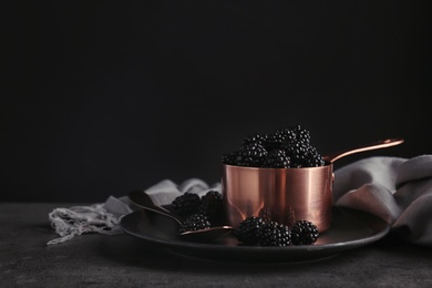 Photo of Saucepan with fresh blackberry on table against dark background. Space for text