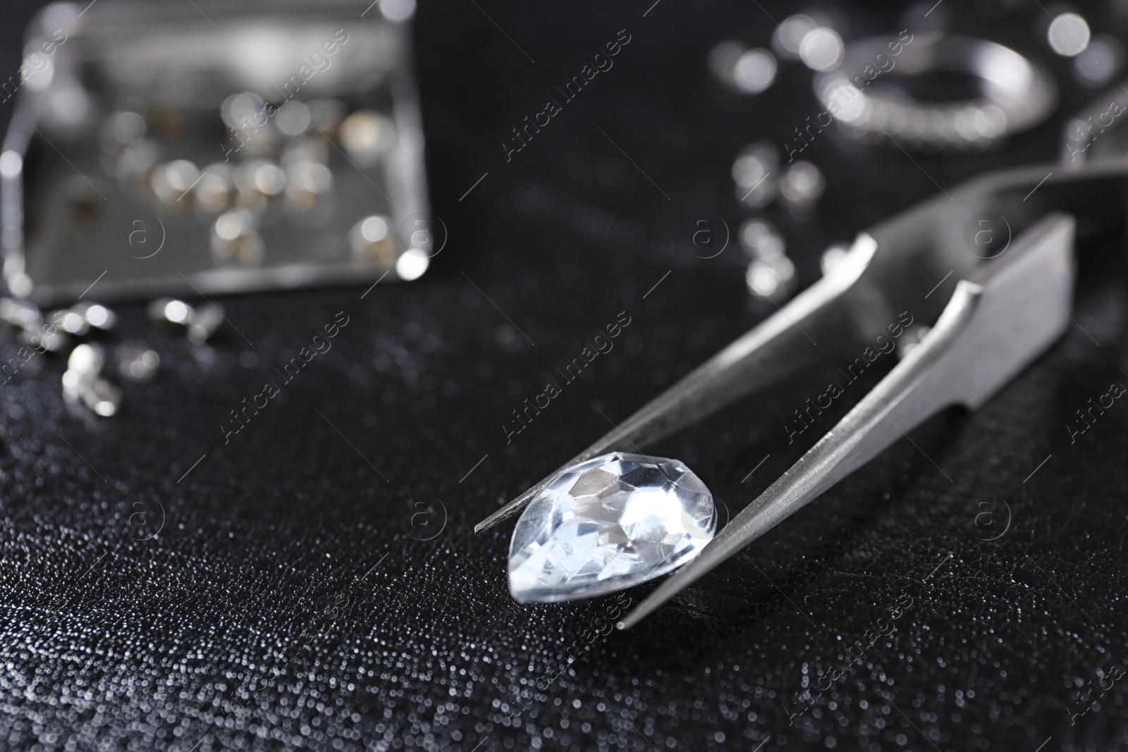 Photo of Jewel and tweezers on black leather surface