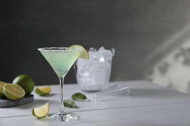 Photo of Delicious Margarita cocktail in glass and limes on white wooden table, space for text