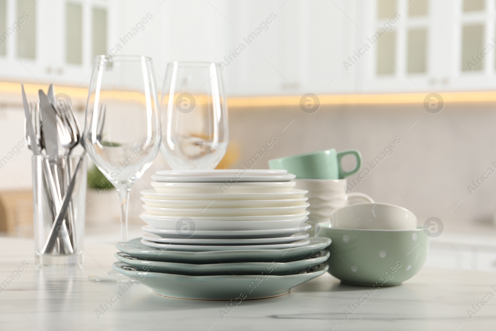 Photo of Many different clean dishware and glasses on white marble table in kitchen