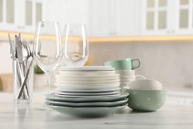 Photo of Many different clean dishware and glasses on white marble table in kitchen