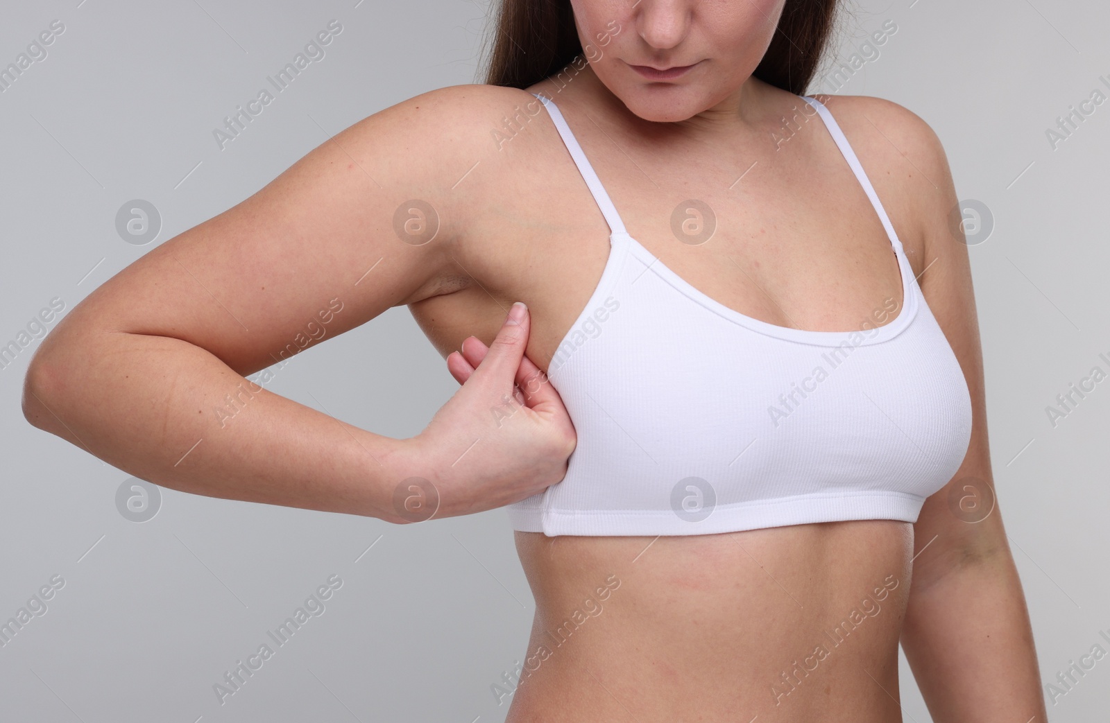 Photo of Mammology. Woman doing breast self-examination on light grey background, closeup