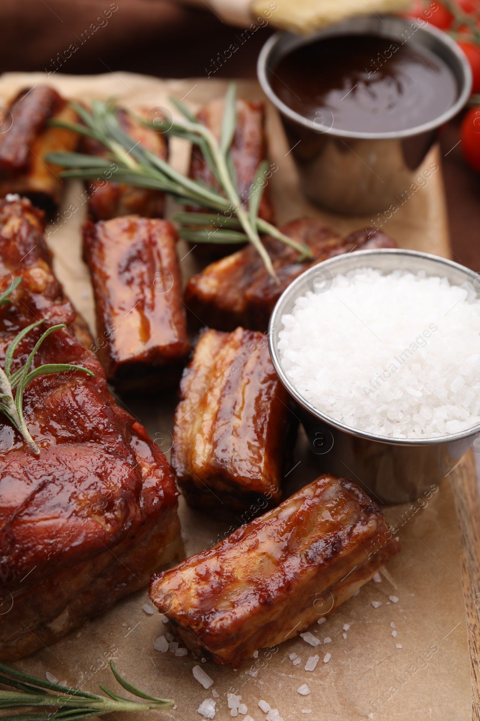 Photo of Tasty roasted pork ribs served with sauce and rosemary on table, closeup