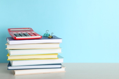 Photo of Stack of hardcover books and calculator on table against color background, space for text