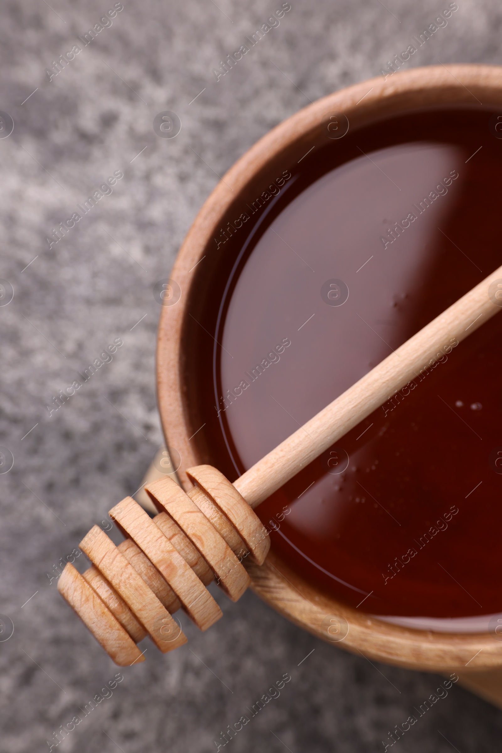 Photo of Delicious honey in bowl and dipper on grey textured table, top view