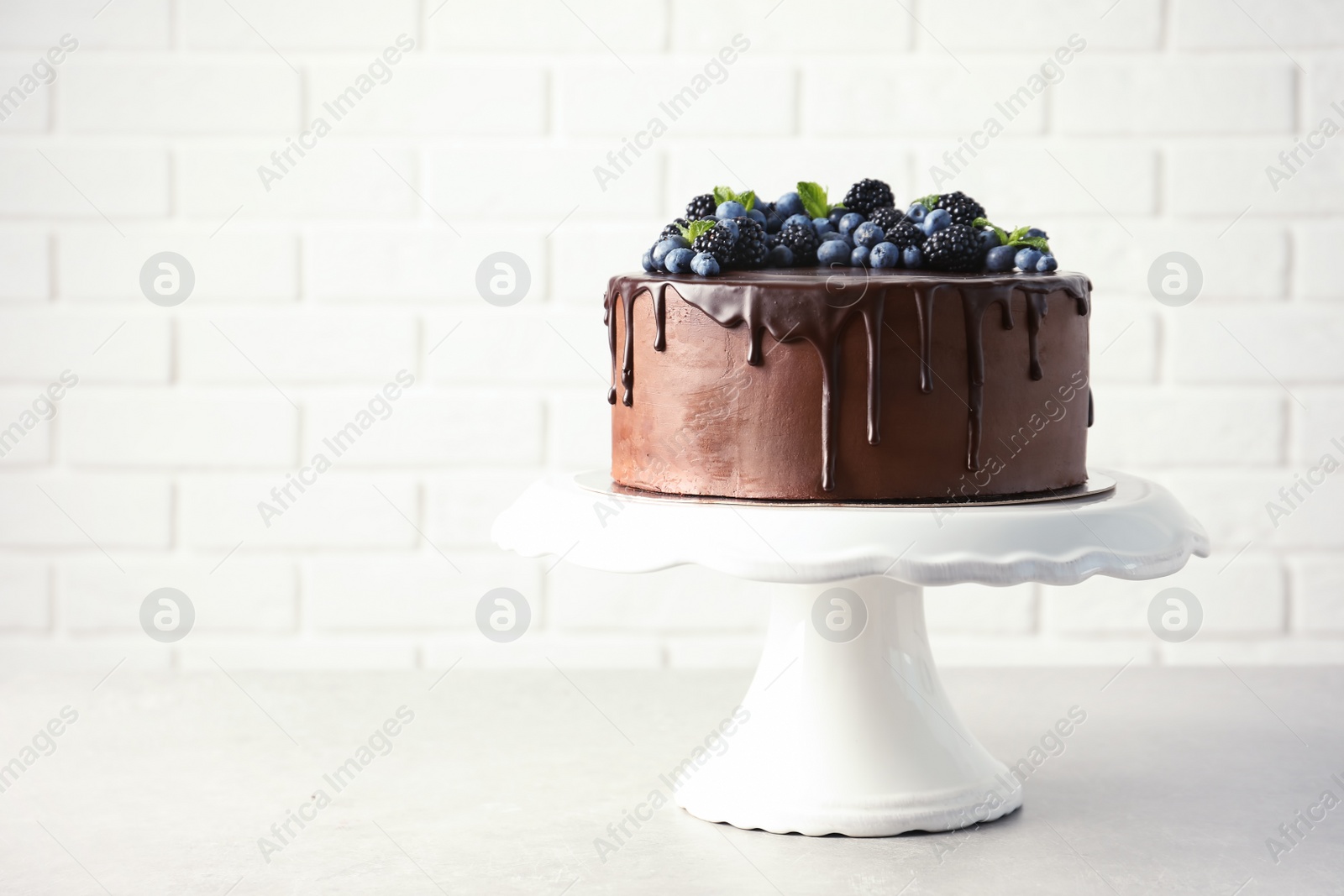 Photo of Fresh delicious homemade chocolate cake with berries on table against brick wall. Space for text