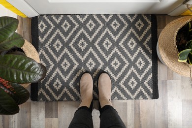 Photo of Woman wearing stylish boots on door mat in hall, top view