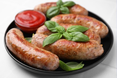 Photo of Plate with tasty homemade sausages, ketchup and basil leaves on white table, closeup