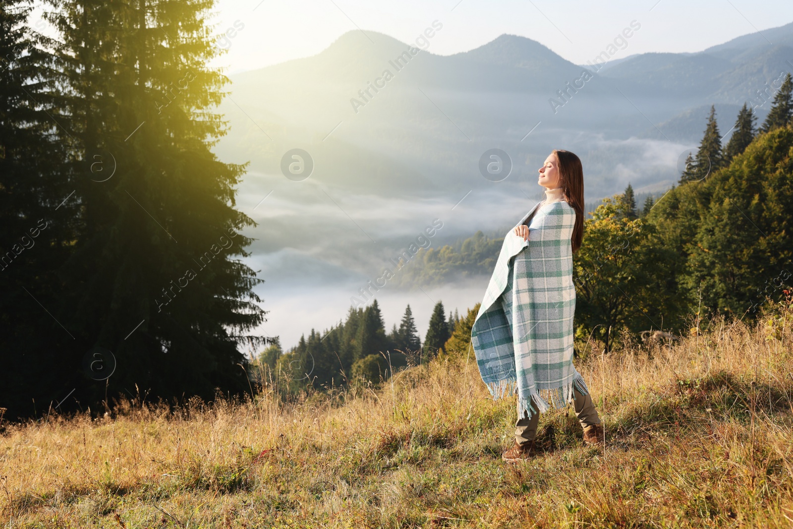 Photo of Woman with cozy plaid enjoying warm sunlight in mountains