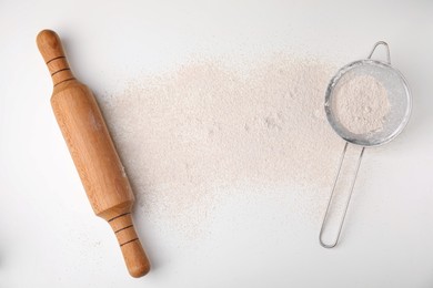 Photo of Flour, rolling pin and sieve on white table, flat lay