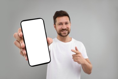 Photo of Handsome man showing smartphone in hand and pointing at it on light grey background, selective focus. Mockup for design