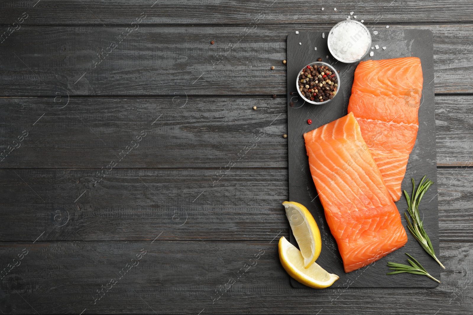 Photo of Slate plate with salmon fillet on black wooden table, flat lay. Space for text