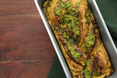 Freshly baked pesto bread in loaf pan on wooden table, top view. Space for text
