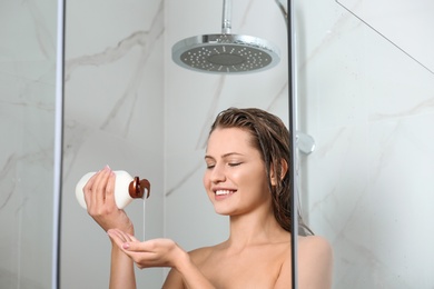 Beautiful young woman with bottle of shampoo in shower at home
