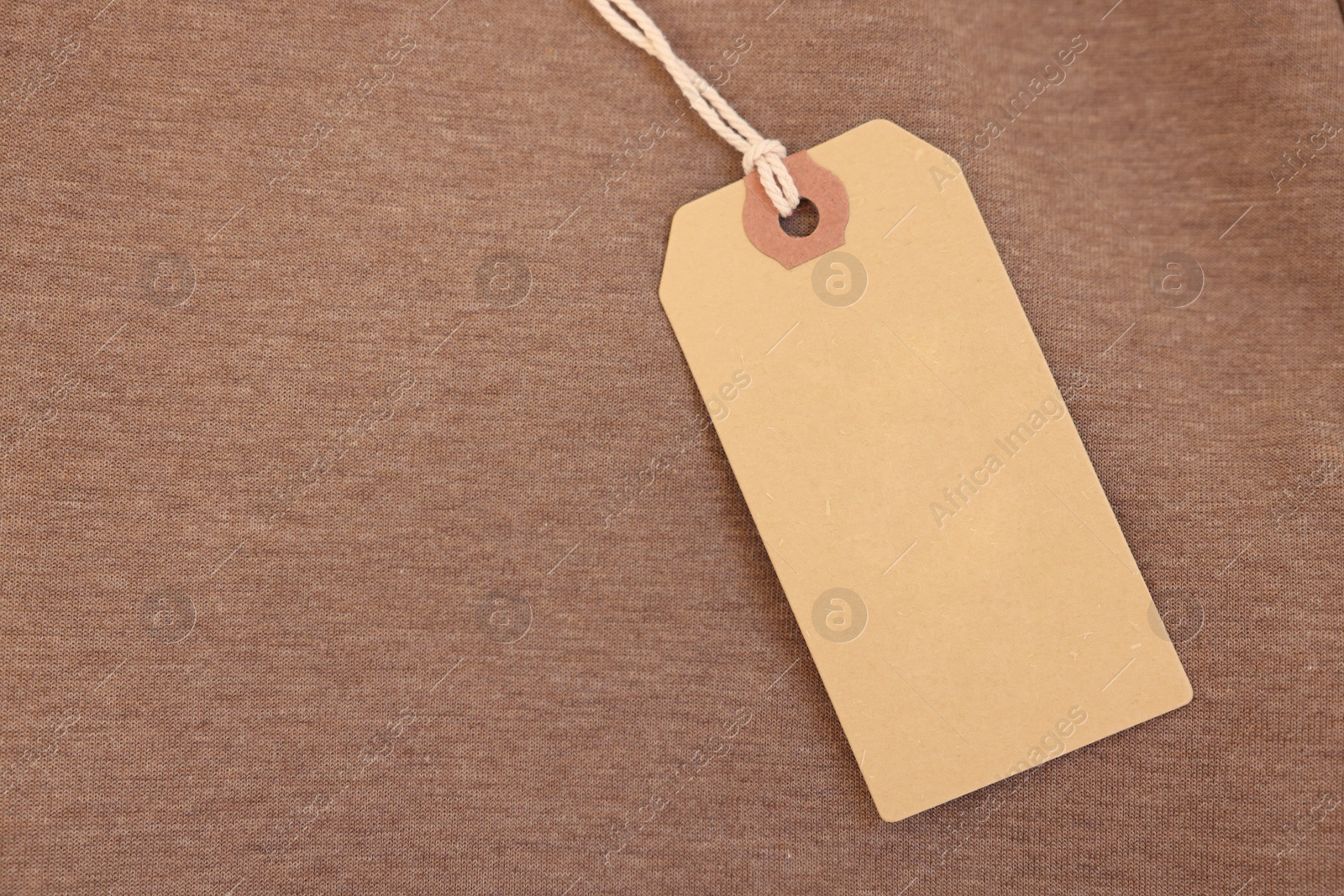 Photo of Cardboard tag on brown garment, top view. Space for text