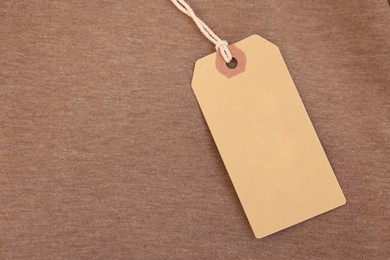 Photo of Cardboard tag on brown garment, top view. Space for text