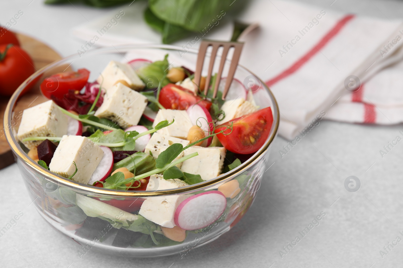 Photo of Bowl of tasty salad with tofu and vegetables on light grey table, closeup. Space for text