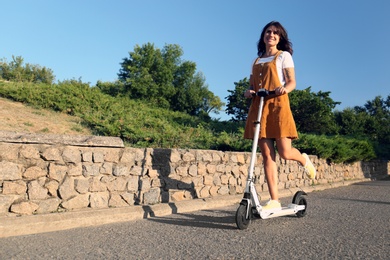 Young woman riding kick scooter along city street